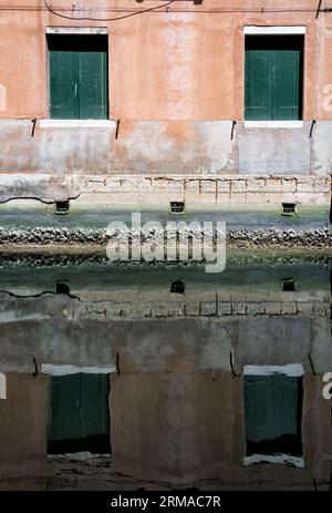 Nahaufnahme Detail mit alten mittelalterlichen Architektur venezianischen Fenster. Reflexion im Wasser eines abgenutzten Backsteinmauergebäudes mit hölzernen Grünläden. Stockfoto
