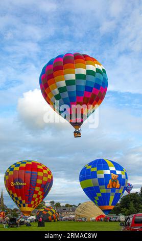 A hot-air balloon with passengers taking off above two other balloons, and others being inflated, during the Strathaven Balloon Festival 2023 in Strat Stock Photo