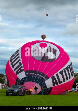 Ein Heißluftballon, der für den Flug aufgepumpt wird, während zwei weitere auf dem Strathaven Balloon Festival 2023 in Strathaven, SC, in die Ferne fliegen Stockfoto