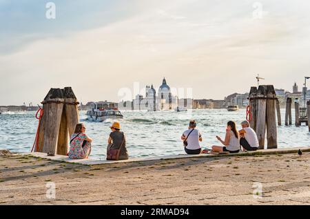 Venedig, Italien - Mai 30 2023: Touristen sitzen am Ufer und genießen die idyllische Szene am Canal Grande in Venedig. Stockfoto