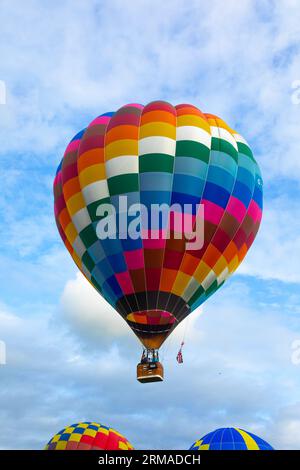 Ein Heißluftballon mit Fluggästen, die während des Strathaven Balloon Festivals 2023 in Strathaven, Schottland, über zwei anderen Ballons starten Stockfoto