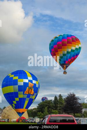 Hot-air balloons taking off, flying and and others being inflated, during the Strathaven Balloon Festival 2023 in Strathaven, Scotland. Stock Photo