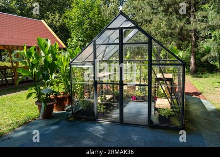 Gewächshaus im Garten. Kleines, kompaktes Glasgewächshaus für den Anbau von Blumen, Gemüse, Setzlingen verschiedener Pflanzen. Gartenarbeit. Wunderschönes Glashaus im Hof. Hobby kein Graben. Stockfoto