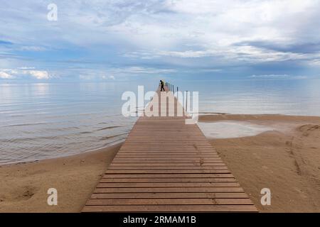 Touristen mit Rucksack zu Fuß auf einem schönen hölzernen Pier und Sandstrand am Kauksi Strand am Peipus See in Estland, Stockfoto