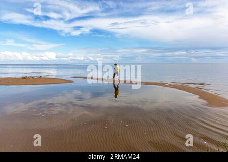 Touristischer Wanderer mit Rucksack, der den wunderschönen Sandstrand Kauksi am Peipus-See an einem klaren sonnigen Tag in Estland erkundet, Stockfoto