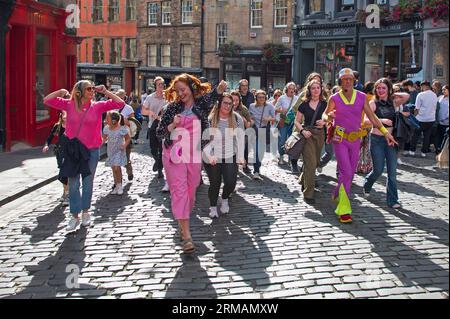 Grassmarket, Edinburgh, Schottland, Großbritannien. 27. August 2023. Die stille Disco unter der Leitung von David für Guru Dudu führt durch Grassmarket und in die Victoria Street im Stadtzentrum. Diese häufigen Veranstaltungen wurden von einigen Einheimischen negativ kommentiert, da die Teilnehmer oft die Lieder auf ihren Kopfhörern laut auf ihren Stimmen singen, andere Passanten sich über die Szene amüsieren. Quelle: Archwhite/Alamy Live News. Stockfoto