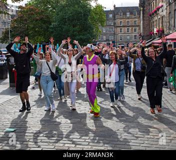 Grassmarket, Edinburgh, Schottland, Großbritannien. 27. August 2023. Die stille Disco unter der Leitung von David für Guru Dudu führt durch Grassmarket und in die Victoria Street im Stadtzentrum. Diese häufigen Veranstaltungen wurden von einigen Einheimischen negativ kommentiert, da die Teilnehmer oft die Lieder auf ihren Kopfhörern laut auf ihren Stimmen singen, andere Passanten sich über die Szene amüsieren. Quelle: Archwhite/Alamy Live News. Stockfoto