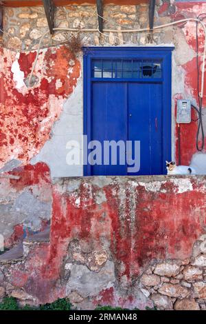 Alte aber schöne alte, blaue Holztür an einem verlassenen Haus mit abgenutztem Gips an den rot-weißen Wänden, auf Hydra Insel, Griechenland, Europa. Stockfoto