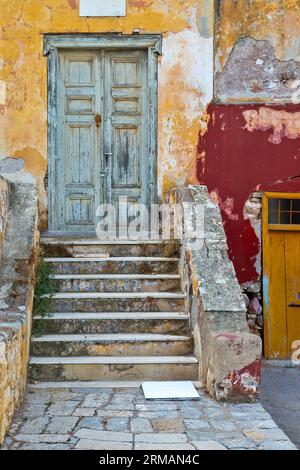 Eingang eines wunderschönen alten Hauses mit hellen, aber alten Farben auf abgenutzten Wänden, auf Hydra Insel, Griechenland, Europa. Stockfoto