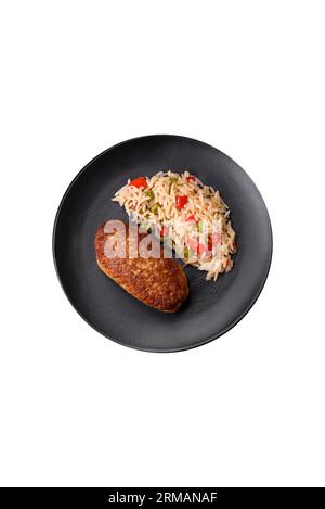 Köstliche gebratene Schnitzel oder Hackfleischbällchen mit Reis, Gemüse, Gewürzen und Kräutern auf dunklem Betonhintergrund Stockfoto