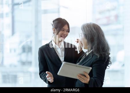 Zwei glückliche Mitarbeiter, die über Finanzberichte auf Tablets diskutieren und gemeinsam an Projekten arbeiten Stockfoto