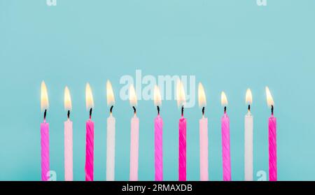 11 rosa und weiße Geburtstagskerzen, die in einer Reihe isoliert auf Blau brennen. „Happy Birthday“-Kartendesign. Untere Randkante. Stockfoto