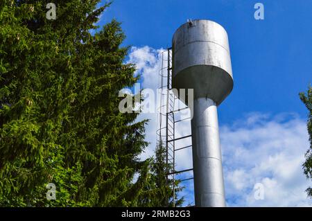 Großer rostfreier Wasserturm aus Eisen, glänzend, aus Metall, für die Versorgung von Wasser mit großer Kapazität, Fass gegen den blauen Himmel und Bäume. Stockfoto