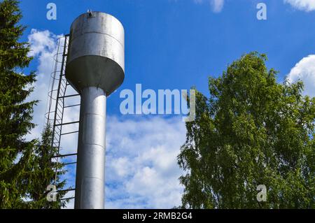 Großer rostfreier Wasserturm aus Eisen, glänzend, aus Metall, für die Versorgung von Wasser mit großer Kapazität, Fass gegen den blauen Himmel und Bäume. Stockfoto