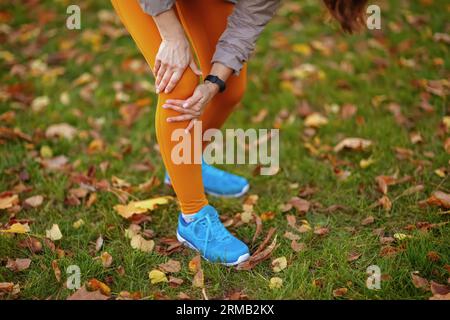 Hello autumn. Closeup on middle aged woman in fitness clothes in the park with knee pain. Stockfoto