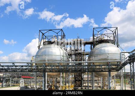 Ein großer, runder, kugelförmiger, glänzender metallischer Hochdruck-Eisen-Lagertank für Ammoniak ist stark mit Rohren und Anlagen in der petrochemischen Industrie Stockfoto