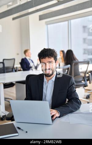 Selbstbewusster, glücklicher junger Geschäftsmann aus Lateinamerika, der mit einem Laptop bei der Arbeit sitzt. Stockfoto