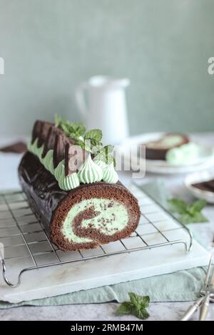 Schokoladen-Minz-Kuchenrolle. Köstliches hausgemachtes Dessert. Frische Minzblätter, grüne Serviette und weißer Teller. Stockfoto