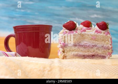 Eine Scheibe Celebration Party Cream und Erdbeeren Kuchen und Tee Kaffee Tasse am Meer Stockfoto