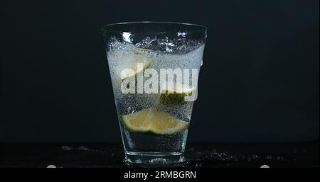 Grüne Zitrusfrüchte, Zitrusfrüchte aurantifolia, fallen in ein Glas Wasser, Stockfoto