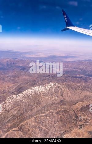 Berge mit Schnee, blauer Himmel - Blick aus dem Flugzeugfenster, Flugzeugflügel FlyDubai Airline - Luftaufnahme von einem Flugzeugfenstersitz Stockfoto