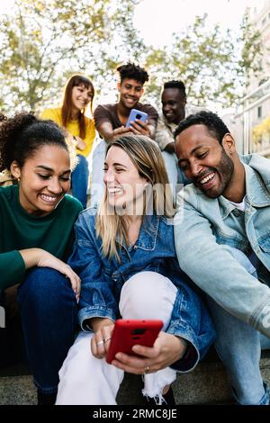 Junge Gruppe von Menschen, die im Freien sitzen und Spaß mit Smartphones haben Stockfoto