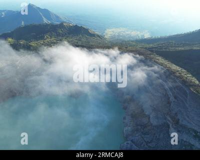 Atemberaubender Blick auf die majestätische Bergkette des Ijen Vulkankraters mit Nebel, klarem See, reflektierendem Himmel und üppigen grünen Wäldern Stockfoto