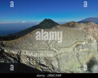 Atemberaubende Berglandschaft des Ijen-Vulkans mit einem Kraterfelsen, üppiger Vegetation, einem Tal und einem klaren blauen Himmel. Stockfoto