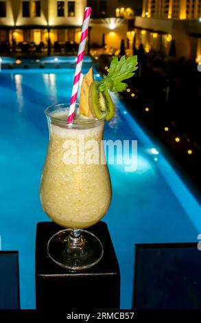 Ein Glas Pina Colada Cocktail mit Strohhalm vor einem blauen Lagunenpool. Kiwi Colada Glas vor einem Nachtpool Hintergrund, Amman Sheraton Hotel Jordan Stockfoto