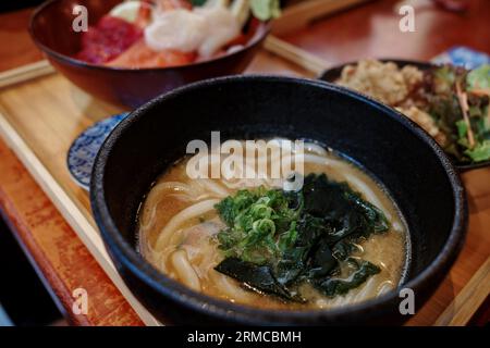 Selektiver Fokus auf Miso-Udon-Nudelsuppe und verschwommener Hintergrund von Sashimi Don, Danburi oder japanischer Reisschale mit verschiedenen rohen frischen Zutaten. Stockfoto