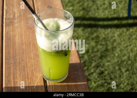 Grüner Smoothie im Glas mit Strohhalm auf einem Holztisch gegen grünes Gras Stockfoto