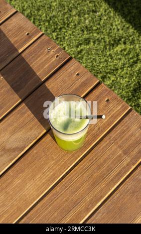 Grüner Smoothie im Glas mit Strohhalm auf einem Holztisch gegen grünes Gras Stockfoto