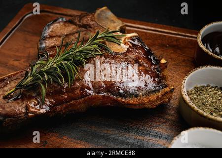 T-Bone-Steak, perfekt gegrillt mit Rosmarin und Gewürzen auf dunklem Holzbrett Stockfoto