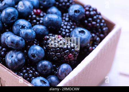 Heidelbeeren und Brombeeren in einer Pappschachtel auf einem Holztisch. Mischung aus blauen Beeren aus nächster Nähe. Stockfoto