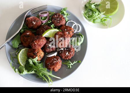 Köstliche frittierte Fleischbällchen mit Raketenblättern und Limettenscheiben auf einem Teller isoliert auf weißem Hintergrund. Ansicht von oben. Stockfoto