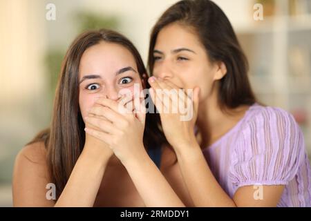 Frau, die ein Geheimnis an das Ohr eines überraschten Freundes zu Hause hängt Stockfoto