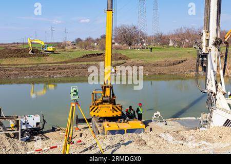 Mobilkran und Bohrmaschine mit Turm, große Ausrüstung zum Bohren in den Boden werden auf Brückenfundament betrieben, im Bau am Fluss Stockfoto