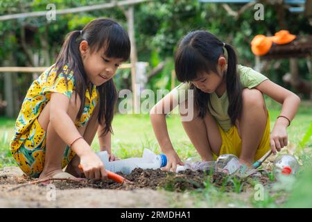 Kleines Mädchen pflanzt Pflanzen in Töpfen aus recycelten Wasserflaschen im Hinterhof. Recyceln Sie Wasserflaschenbecher, Gartenaktivitäten für Kinder. Recyclin Stockfoto