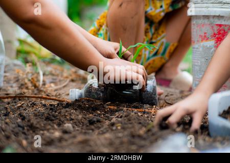 Kleine Mädchen und Mom bauen Pflanzen in Töpfen aus recycelten Wasserflaschen im Hinterhof an. Recyceln Sie Wasserflaschenbecher, Gartenaktivitäten für Kinder. Empy Stockfoto