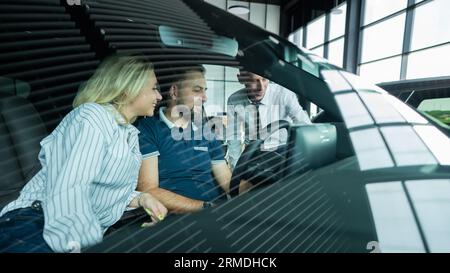 Der Verkäufer demonstriert den Käufern das Fahrzeuginnere. Ein weißes Paar sucht sich ein Auto aus. Stockfoto