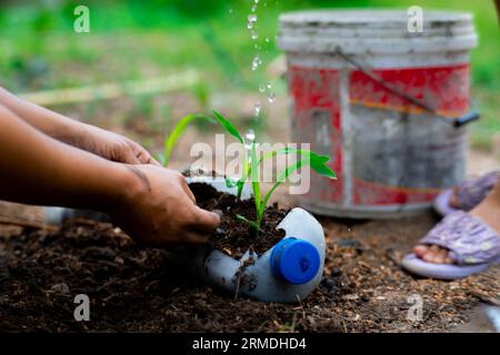 Kleine Mädchen und Mom bauen Pflanzen in Töpfen aus recycelten Wasserflaschen im Hinterhof an. Recyceln Sie Wasserflaschenbecher, Gartenaktivitäten für Kinder. Empy Stockfoto