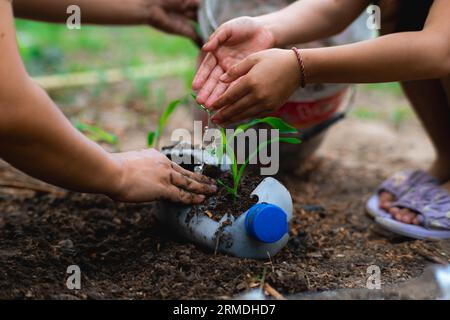 Kleine Mädchen und Mom bauen Pflanzen in Töpfen aus recycelten Wasserflaschen im Hinterhof an. Recyceln Sie Wasserflaschenbecher, Gartenaktivitäten für Kinder. Empy Stockfoto