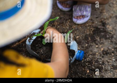 Kleine Mädchen und Mom bauen Pflanzen in Töpfen aus recycelten Wasserflaschen im Hinterhof an. Recyceln Sie Wasserflaschenbecher, Gartenaktivitäten für Kinder. Empy Stockfoto