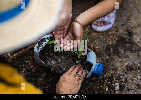 Kleine Mädchen und Mom bauen Pflanzen in Töpfen aus recycelten Wasserflaschen im Hinterhof an. Recyceln Sie Wasserflaschenbecher, Gartenaktivitäten für Kinder. Empy Stockfoto