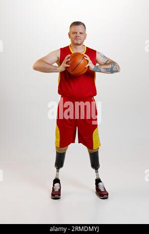 Attraktiver Mann mit Beinprothesenbehinderung stehend mit orangenem Basketballkorb. Inklusiver Sport für Menschen mit Behinderungen. Stockfoto