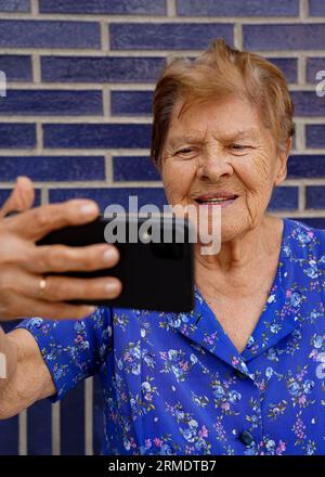 Glückliche alte Frau aus den 90ern, die die Handy-App für Videoanrufe nutzt, lachend, während sie lustige Videos ansieht Stockfoto