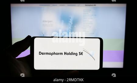 Person mit Smartphone mit Logo des deutschen Pharmaunternehmens Dermapharm AG auf dem Bildschirm vor der Website. Konzentrieren Sie sich auf das Display des Telefons. Stockfoto