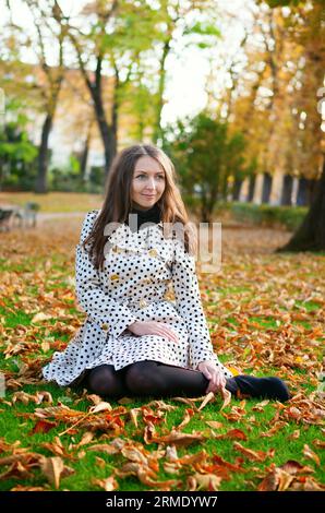 Mädchen, das an einem Herbsttag auf dem Boden im Park sitzt Stockfoto