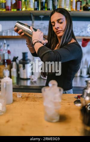 Die junge Barfrau bereitet einen alkoholischen Cocktail in der Bar zu Stockfoto