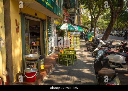 Ein traditioneller Street Food Stand, der Reisnudeln mit Schnecken oder Tofu neben Motorrädern verkauft, die auf dem Bürgersteig im Zentrum von Hanoi, Vietnam, geparkt sind. Stockfoto